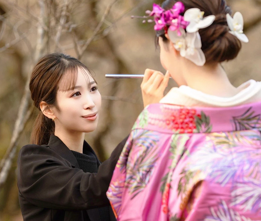花の髪飾りと着物をまとった女性に、ブラシでメイクを施す様子
