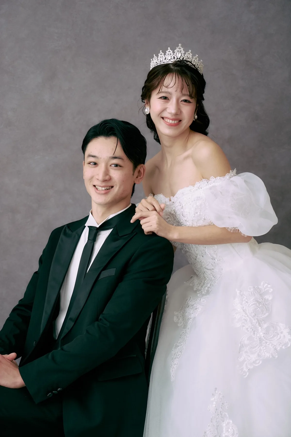 ティアラと白いドレスをまとった花嫁が、タキシード姿の新郎に寄り添うポートレート