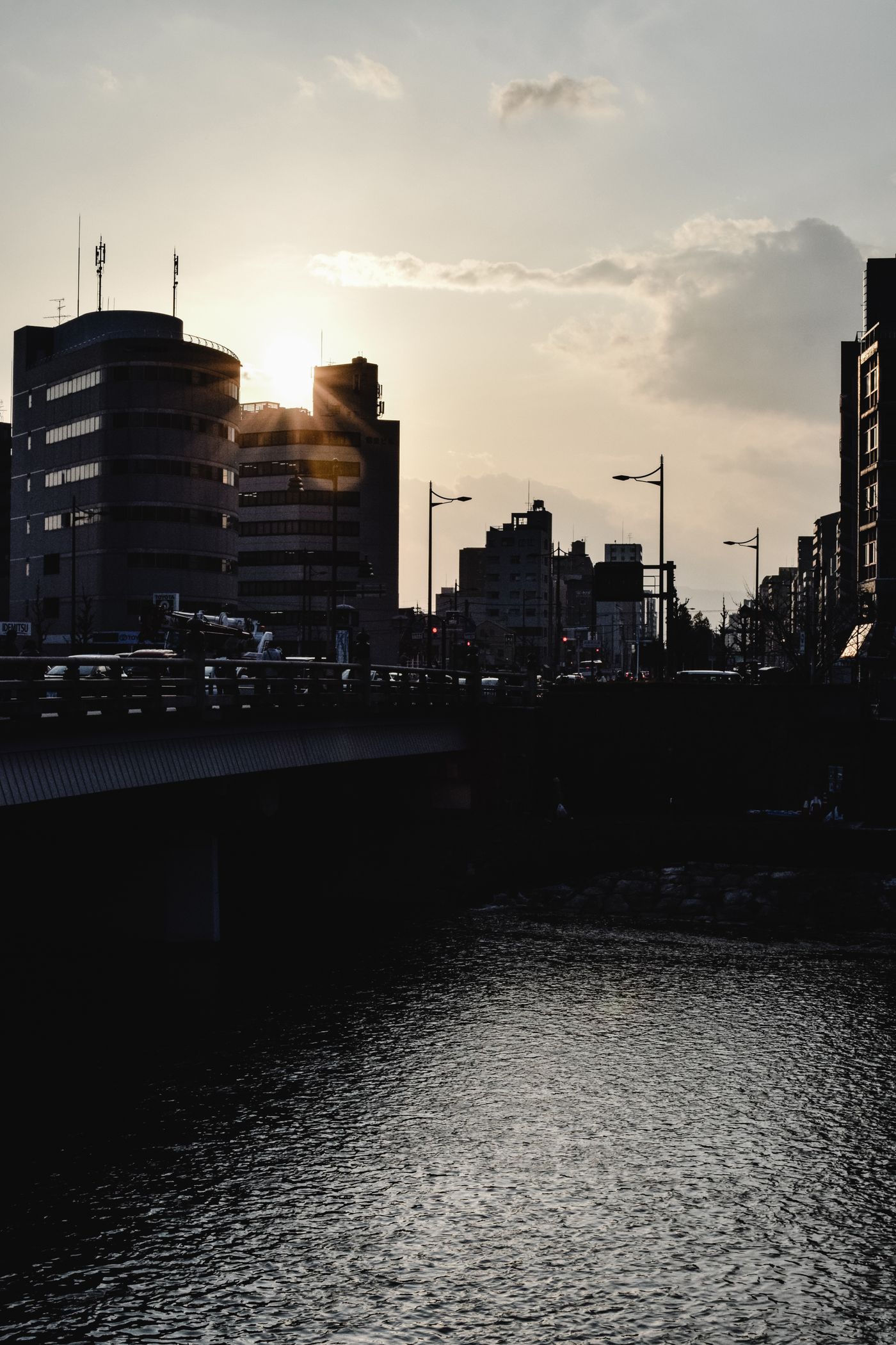 京都の川沿いの建物の間から夕日が差し、水面が光る風景